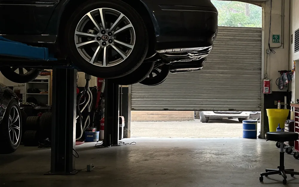 A car raised on a two-post lift in a two-bay workshop.