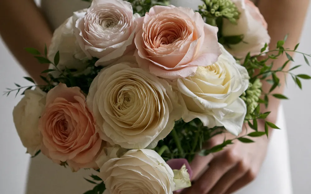 A loose garden-style bridal bouquet of cream and blush roses held at the waist.