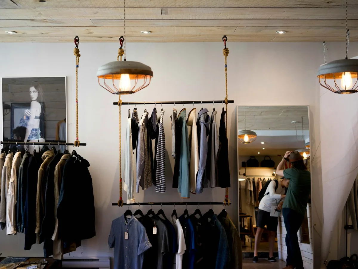 Interior of a wholesale clothing showroom: garment rails under warm pendant lighting, a buyer looking through stock at the back.