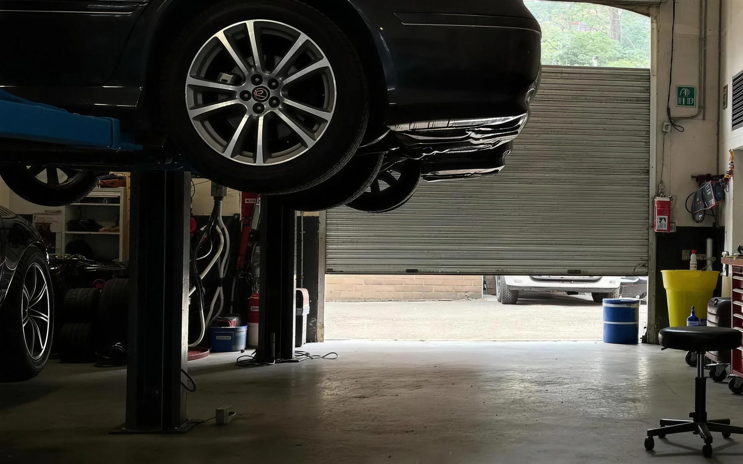 A car raised on a two-post lift in a two-bay workshop.