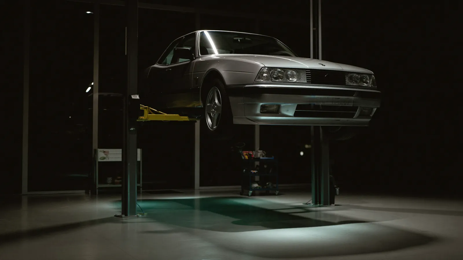 A car raised on a two-post lift in a dimly lit workshop