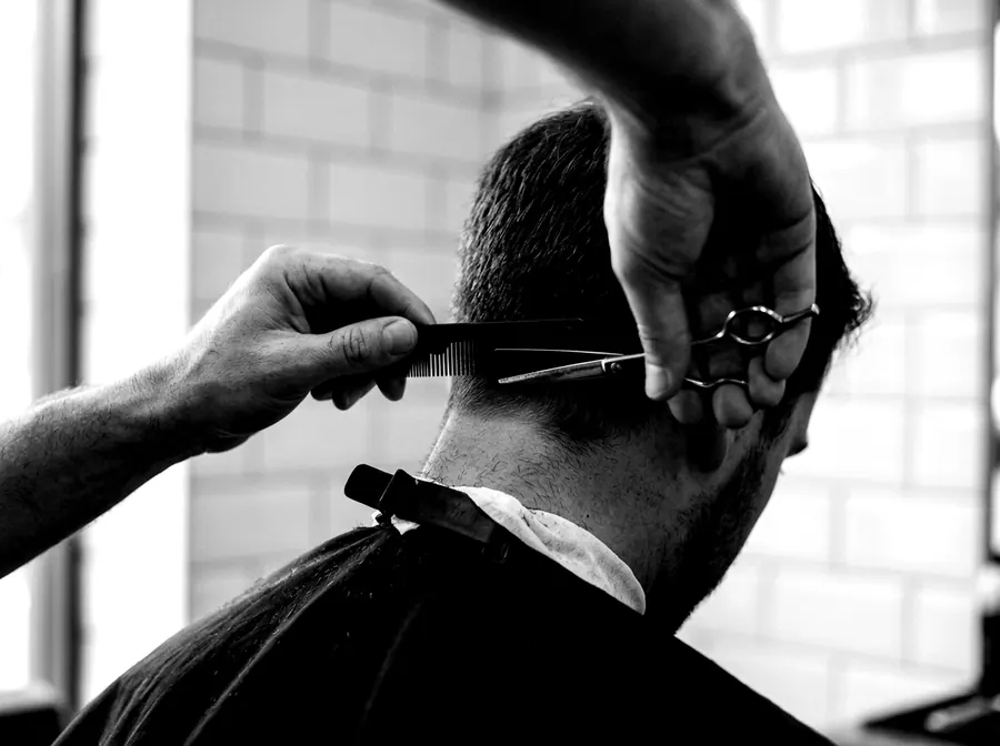 A barber's hands using scissors and comb at the nape of a customer's neck.