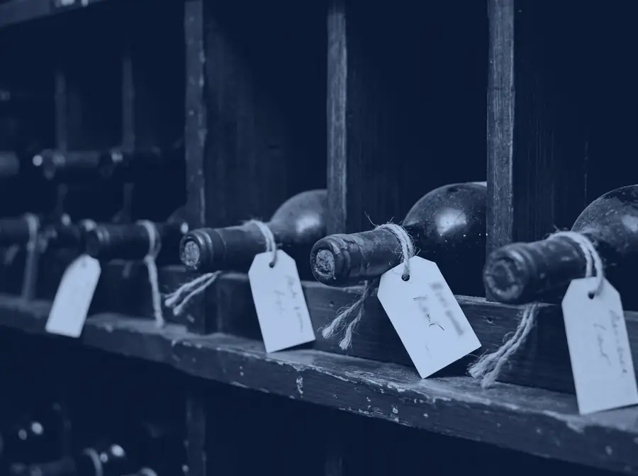 Handwritten card tags tied to the necks of bottles in dark timber racking.