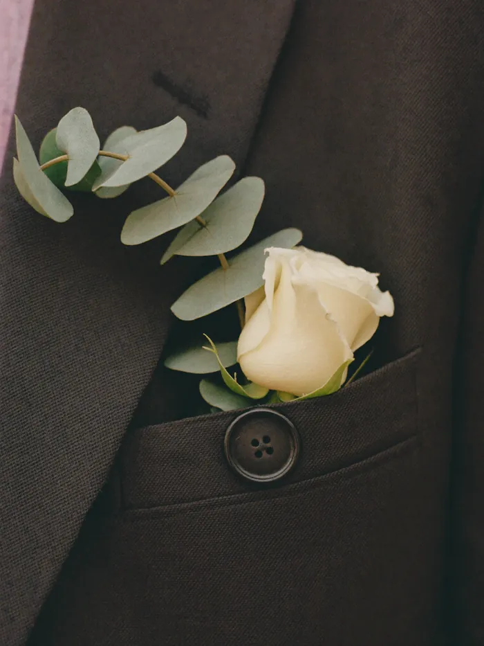 A single cream rose buttonhole pinned to a charcoal lapel