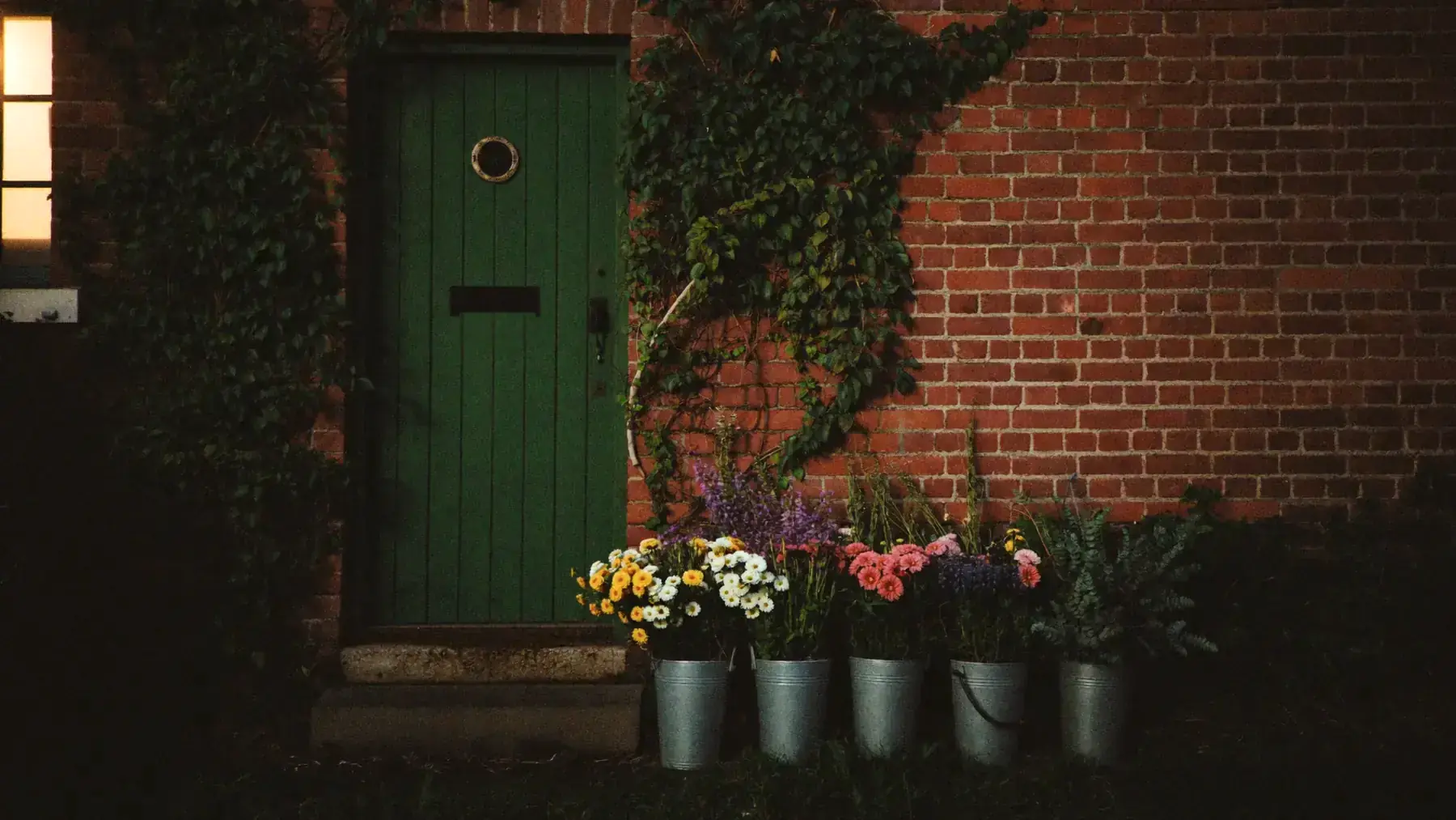 Buckets of cut flowers on the step of a green florist's door in an ivy-covered brick wall