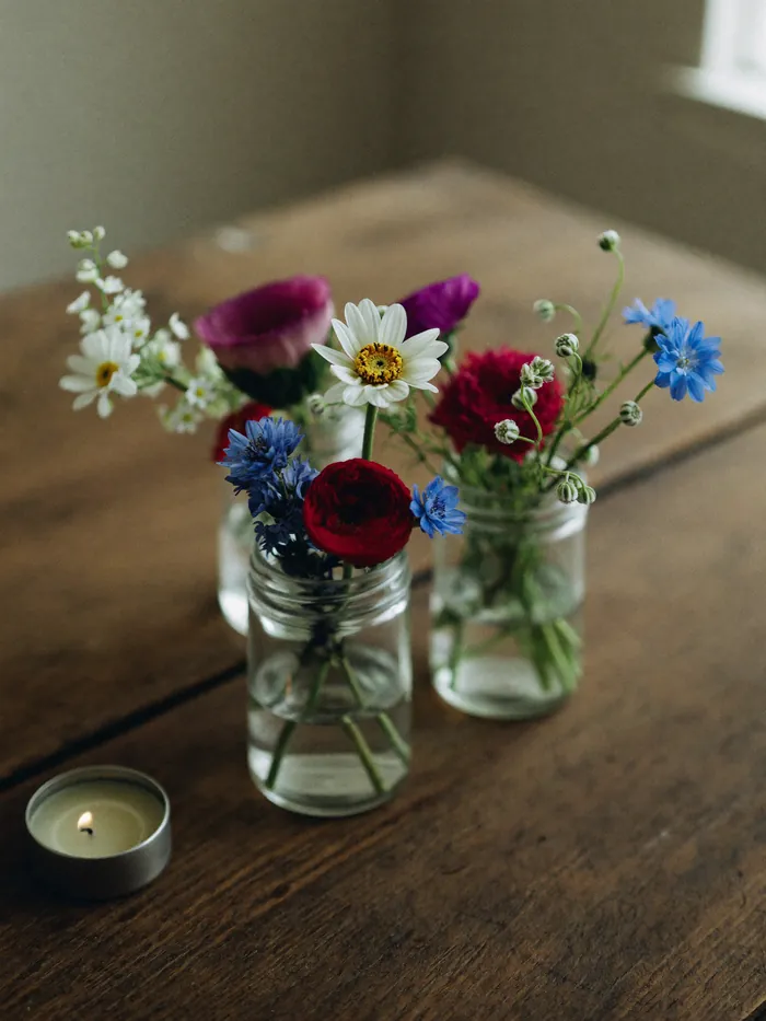 Three small jars of garden flowers clustered on a wooden table