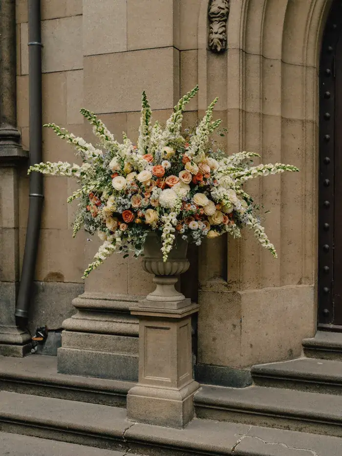 A tall pedestal urn of cream and green flowers beside a stone doorway