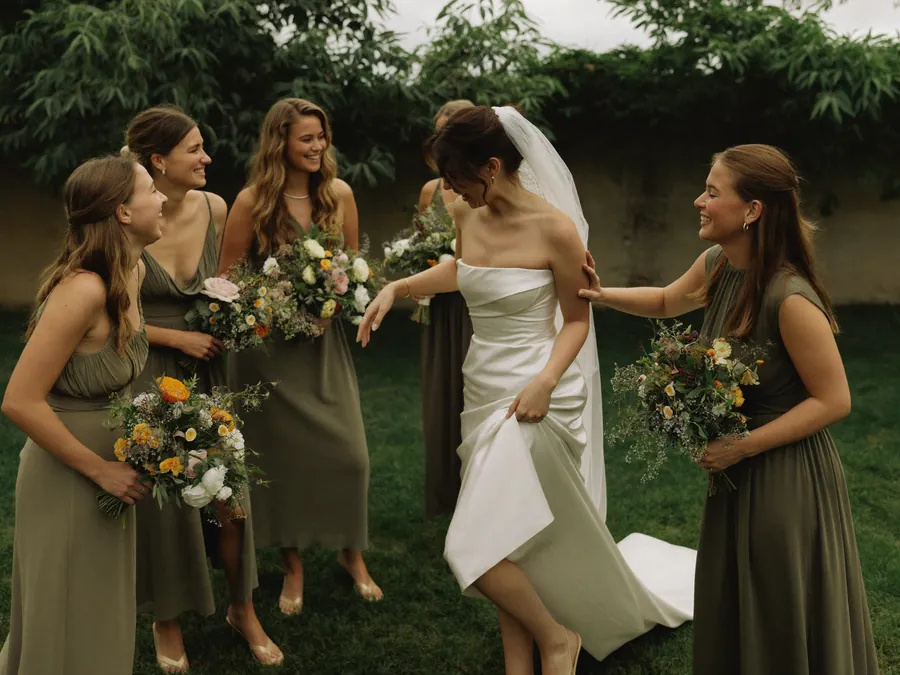 A bride and her bridesmaids laughing together in a walled garden