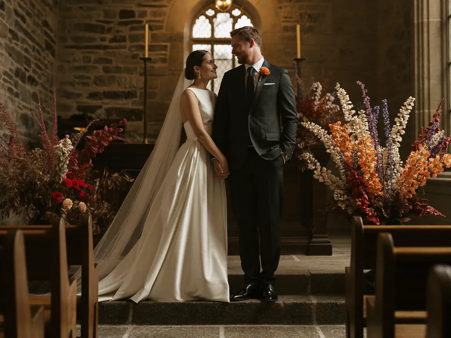 A bride and groom at a church altar between tall autumn arrangements