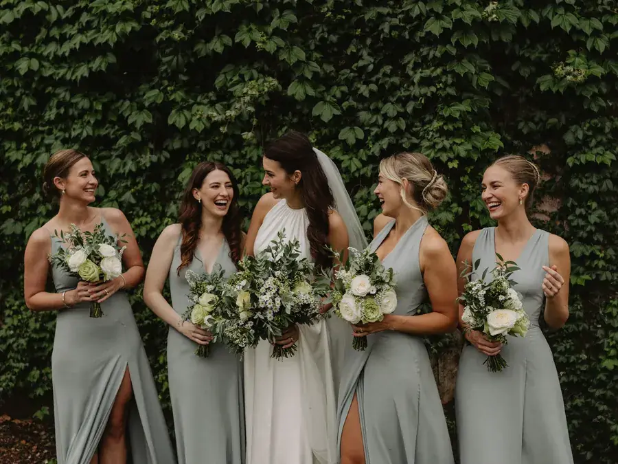 A bride and four bridesmaids in blue against a wall of ivy
