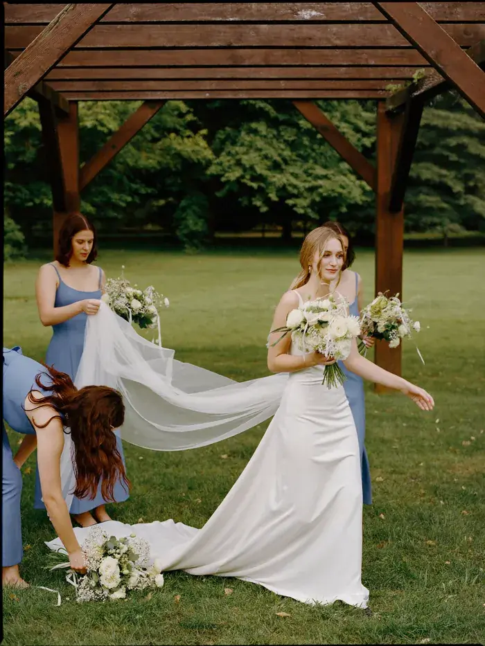 A bride under a timber pergola dressed with cream flowers